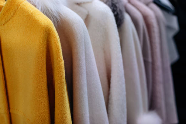 Yellow and white fur coats hanging in a row on hangers in a winter clothing luxury boutique for women
