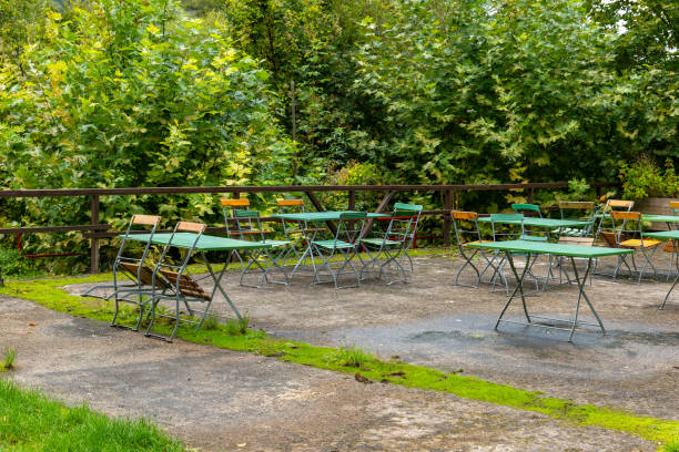 istock Empty tables and chairs sit in an outdoor seating area surrounded by greenery 2178367093