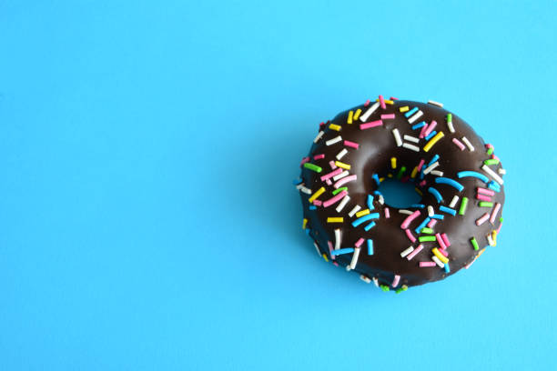 a chocolate donut with colorful sprinkles on a blue background copy space