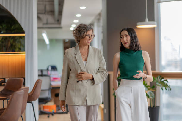 istock Young female business developer walking and engaging in conversation with a strategy expert in a modern office. Gaining valuable advice and insights from an experienced professional. Teamwork, mentorship, and innovation drive the success. 2178376740