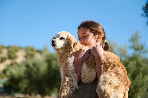 A cheerful girl embraces her golden retriever with joy under a clear blue sky. The scene radiates happiness and innocence, embodying the pure bond between humans and dogs.