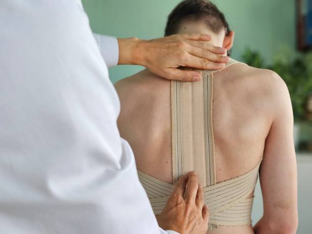 Doctor putting a medical tape on the back of a patient during a rehabilitation session in a clinic Doctor putting a medical tape on the back of a patient during a rehabilitation session in a clinic. Doctor putting corset on back of teenager patient closeup. Spinal curvature treatment kyphosis stock pictures, royalty-free photos & images