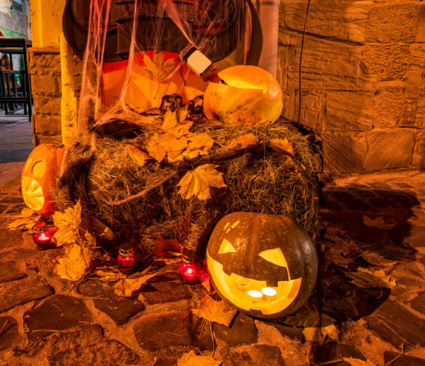 istock Halloween decorations - Jack-o'-lanterns - carved pumpkins, burning candles, hay bale, fallen maple leaves 2178382906