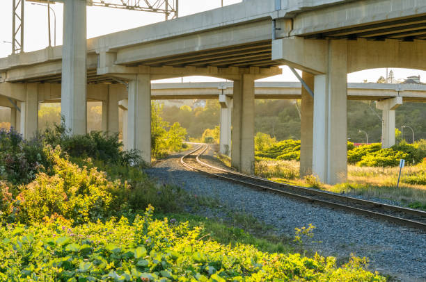 Empty winding railway track passing under a highway in a suburban area at sunset in autumn. Saint John, NB, Canada.