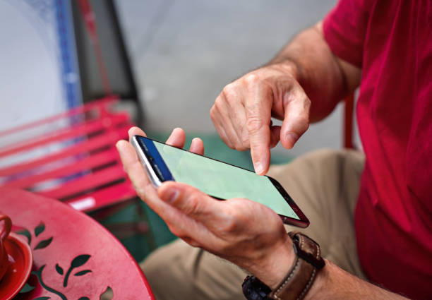 Hands hold and operate a smartphone with a green screen. Person in red sweater sits at a colorful outdoor table, using a banking or financial app to check account information.