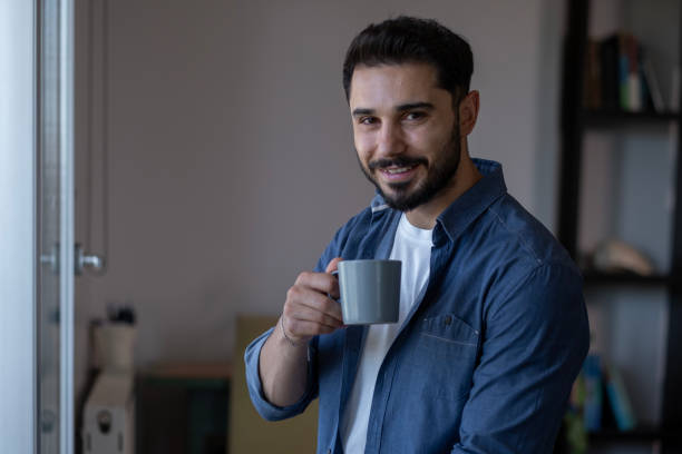 istock Young bearded man drinking coffee with coffee cup in hand looking at camera 2178395924
