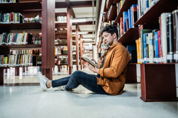 istock Mid adult man reading book at library 2178398697