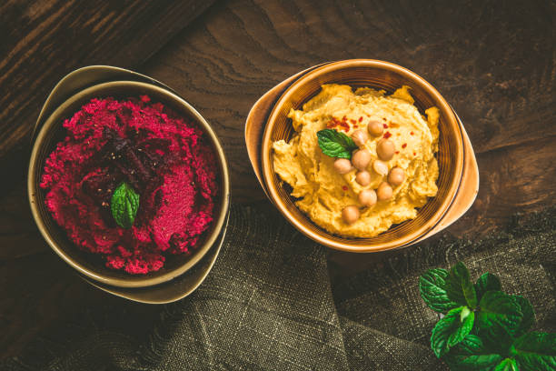Bowls with beetroot hummus and chickpea hummus on a rustic dark wooden background, top view