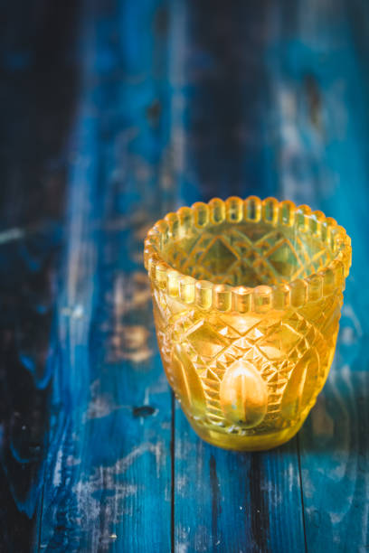 Yellow glass with tea light on blue wooden table, vertical with copy space