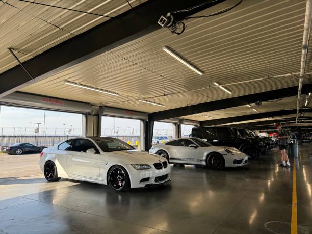 Clarksville, TN, USA - September 21, 2024: A white BMW M3 is parked in a garage. There are other cars in the background, including a Porsche 911 and several SUVs. The garage has fluorescent lights and a concrete floor.