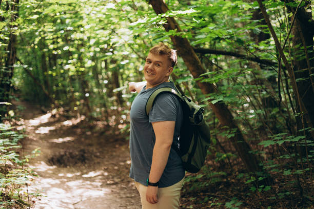 istock Smiling 30s man, with his tourist backpack is standing in a forest. Man points finger at copy space, rest in forest, outdoor, close up. Hiking, active lifestyle, adventure and tourism, people emotions 2178420098