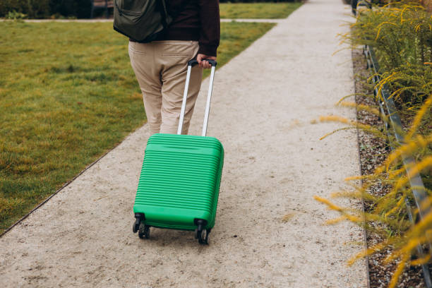 istock Unrecognizable man pulling green suitcase outdoors. Rear view. Copy space. Man walking on the street with travel bag. 2178420168