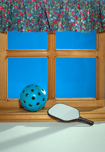 istock Blue Pickleball on window ledge with curtain and Pickleball paddle. 2178428770