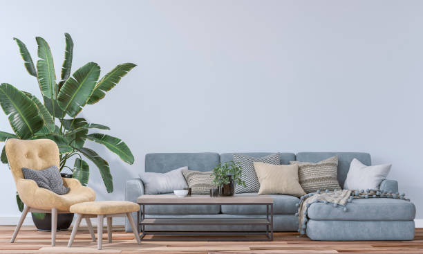 istock A modern living room with a light blue sofa, table with decoration, a mustard boho lounge chair with ottoman and a potted plant on hardwood floor and in front of a white wall background with copy space 2178429666