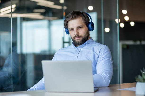 istock Focused Man with Headphones Working on Laptop at Office Desk 2178442577