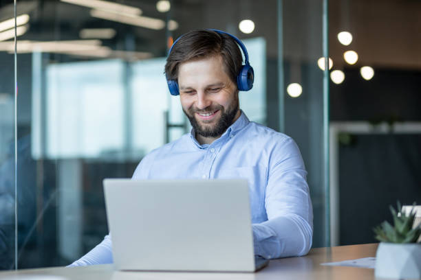istock Happy Man Working on Laptop With Headphones in Modern Office 2178442583