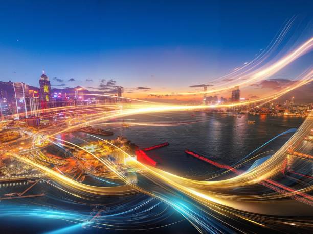 A cityscape with skyscrapers illuminated at night, with long exposure light trails from passing vehicles creating a mesmerizing display over the harbor.