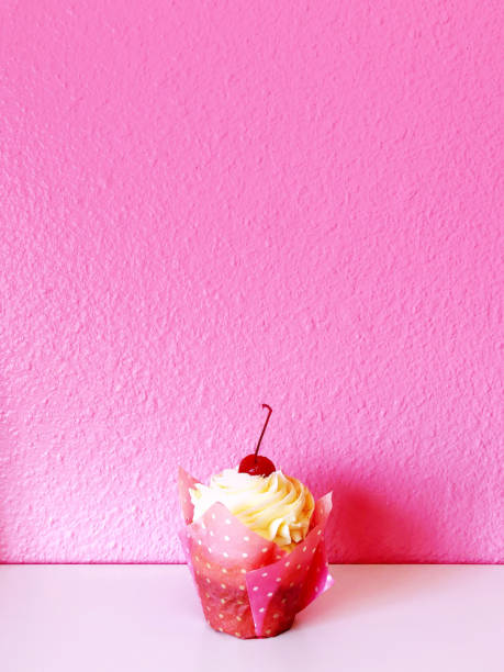 This charming cupcake features a luscious cherry perched atop a fluffy frosting, beautifully contrasted against a soft pink background. The white countertop adds a touch of elegance, while the pink and white polka dot cupcake liner adds a playful, whimsical flair. Perfect for any dessert lover, this image captures the joy of indulgence and the art of baking.