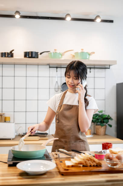 istock A charming Asian woman is talking on the phone while cooking in the kitchen. 2178461210