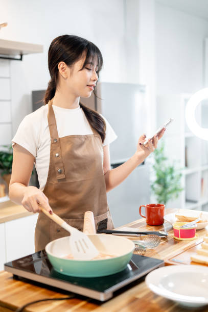 istock A happy Asian woman is holding her smartphone while cooking in the kitchen. 2178461226