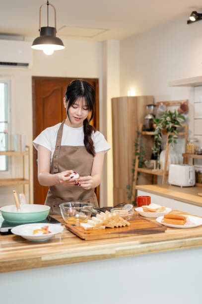 istock A pretty, happy young Asian woman is enjoying cooking in the kitchen, cracking an egg into a bowl. 2178461237
