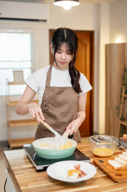 istock A happy Asian woman is cooking in the kitchen, making scrambled egg in a pan for her breakfast. 2178461242