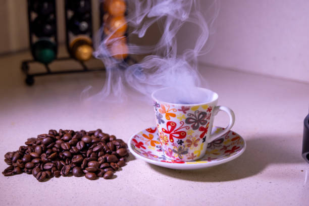 White cup of hot espresso with steam and roasted coffee beans on dark black background
