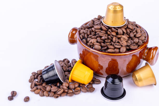 istock Brown bowl filled with coffee beans, topped with a coffee capsule, surrounded by beans and colorful capsules on a white background 2178472511