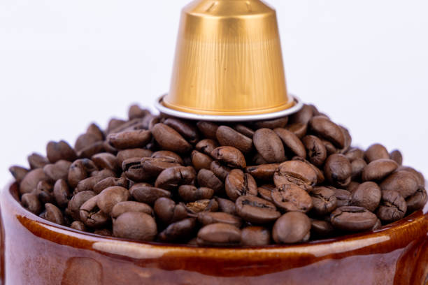 istock Brown bowl filled with coffee beans with a coffee capsule on top, placed on a white background. Close-up view highlighting natural textures 2178473434