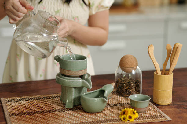 Woman pouring hot water in tea pot while standing in the kitchen