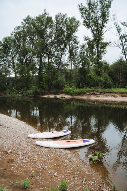 istock Enjoy a tranquil riverside view with two paddleboards resting on the shore, surrounded by lush greenery and a serene atmosphere perfect for relaxation and outdoor leisure 2178480644