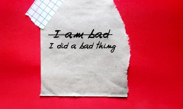 Torn paper note on red background with handwritten text I AM BAD changed to I DID A BAD THING, to overcome low self worth , take responsibility for mistakes, but not degrade themselves