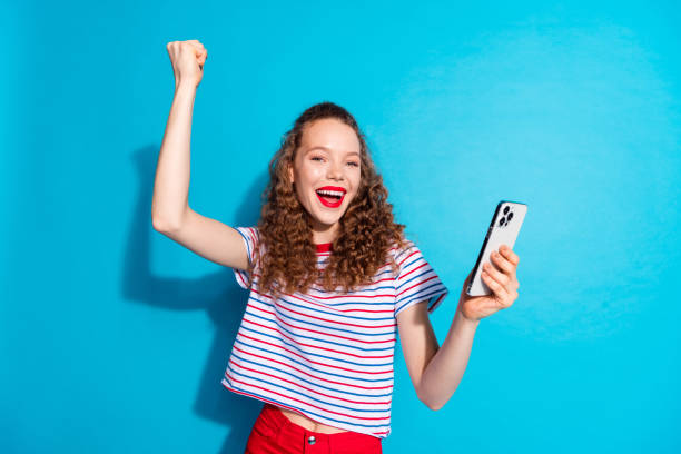 istock Excited young woman celebrating success while using smartphone against a vibrant blue background 2178489274