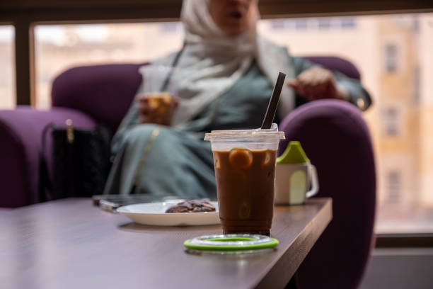 Chilled iced coffee served in a plastic cup with a black straw, accompanied by a chocolate cookie on a white plate. Perfect for a cozy coffee break