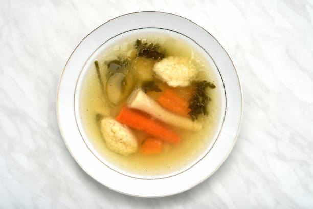 Homemade chicken soup with dumplings, carrots, root and leaves of parsley in the white plate