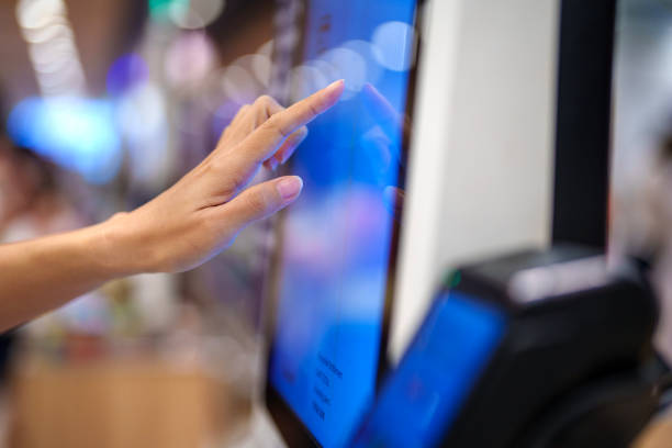 A side view of an adult interacting with a touch screen display at a kiosk machine in a grocery store.