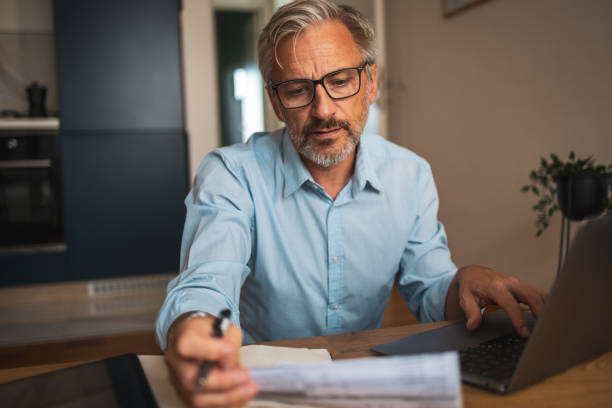istock Mature man reviewing financial documents at home on a laptop 2178501161