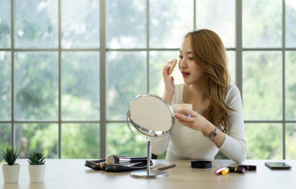 istock A woman is happily applying makeup while looking in a mirror at a table with various beauty products. 2178502263