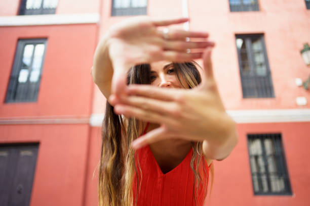 A striking and captivating image of a woman skillfully, using her hands to perfectly frame a dynamic and expressive pose against a vibrant and lively urban backdrop filled with colors and energy