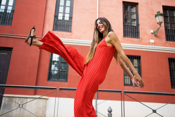 A cheerful woman wearing a bright, vibrant red jumpsuit strikes a fun and playful pose against an eyecatching, colorful urban backdrop that adds to the lively atmosphere of the scene