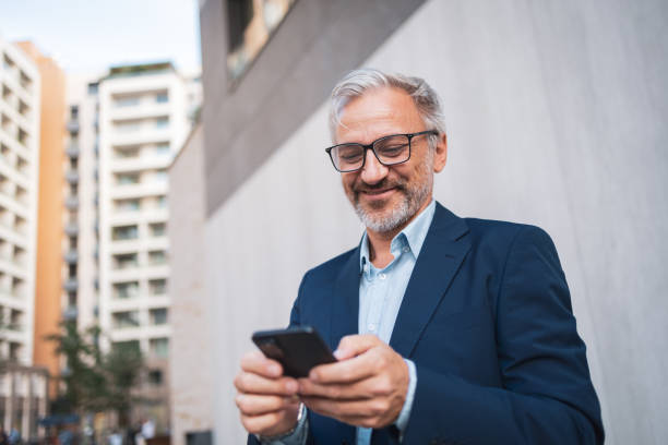 istock Smiling businessman using smartphone outside modern office building 2178507045