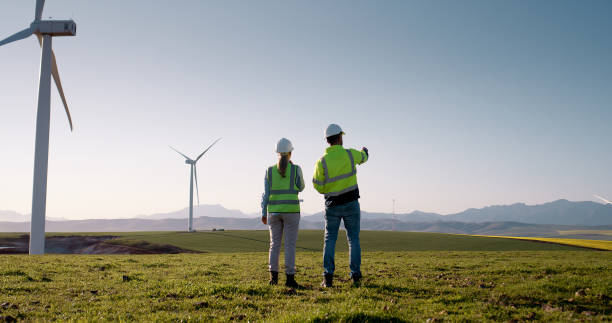 Business people, electrical engineers and discussion with wind turbine for clean, renewable energy or reproduction system. Back view, man and woman with eco friendly resources for power generation