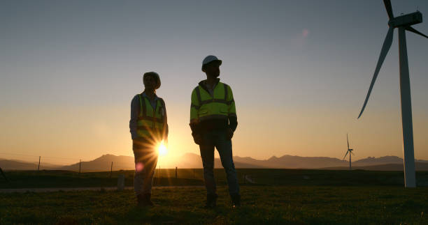 istock Inspection, engineer and team by windmill at sunset for power station maintenance, planning or discussion. Man, woman and wind turbine for electricity generator, construction or clean energy at farm 2178507881