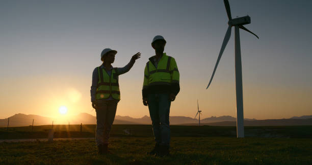istock Planning, engineer and team by wind farm at sunset for power station maintenance, inspection and discussion. Man, woman and windmill for electricity generator, construction and clean energy outdoor 2178507899
