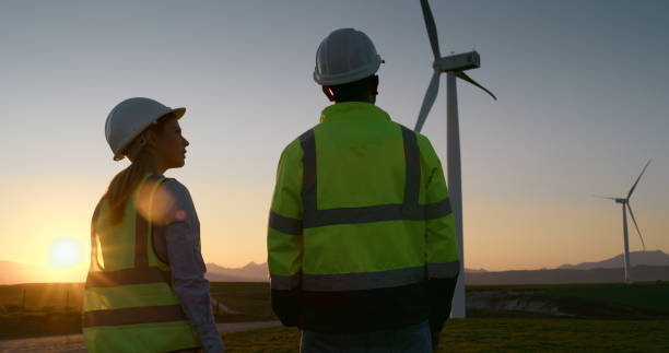 istock Sunset, engineer and team at wind farm for power station maintenance, construction and planning. Man, woman and turbine for electricity generator, green energy and back for inspection or discussion 2178507909