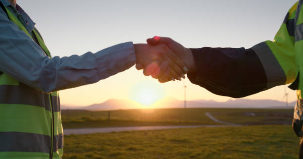 Closeup, engineer and handshake with sunset for renewable energy or eco friendly power in nature. Business people, colleagues or contractors shaking hands for b2b, alternative resources or production