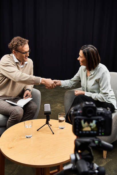 A journalist warmly greets an invited guest during an engaging podcast conversation on set.