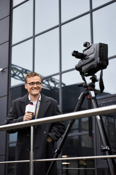 istock Journalist wearing glasses and coat reports news outdoors with a microphone in hand 2178512558