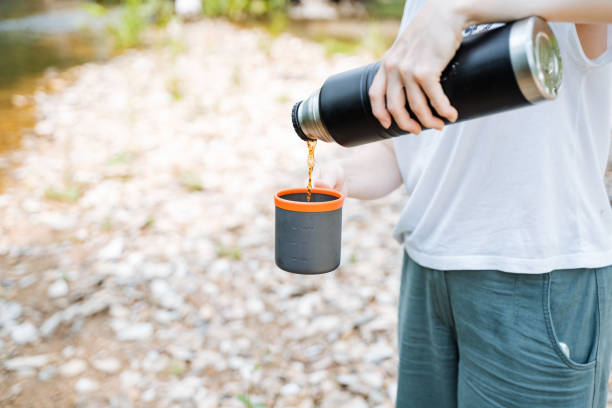 istock A person outdoors pours a beverage into a cup from a thermos during camping or hiking, enjoying a moment of relaxation in nature, amidst a scenic forest or woodland setting 2178520446