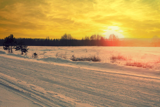 Winter rural landscape. Country road covered with snow at sunset